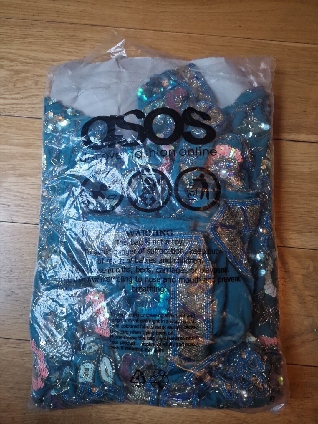 Floral embellished oversized jacket from ASOS folded inside clear plastic packaging on wooden floor