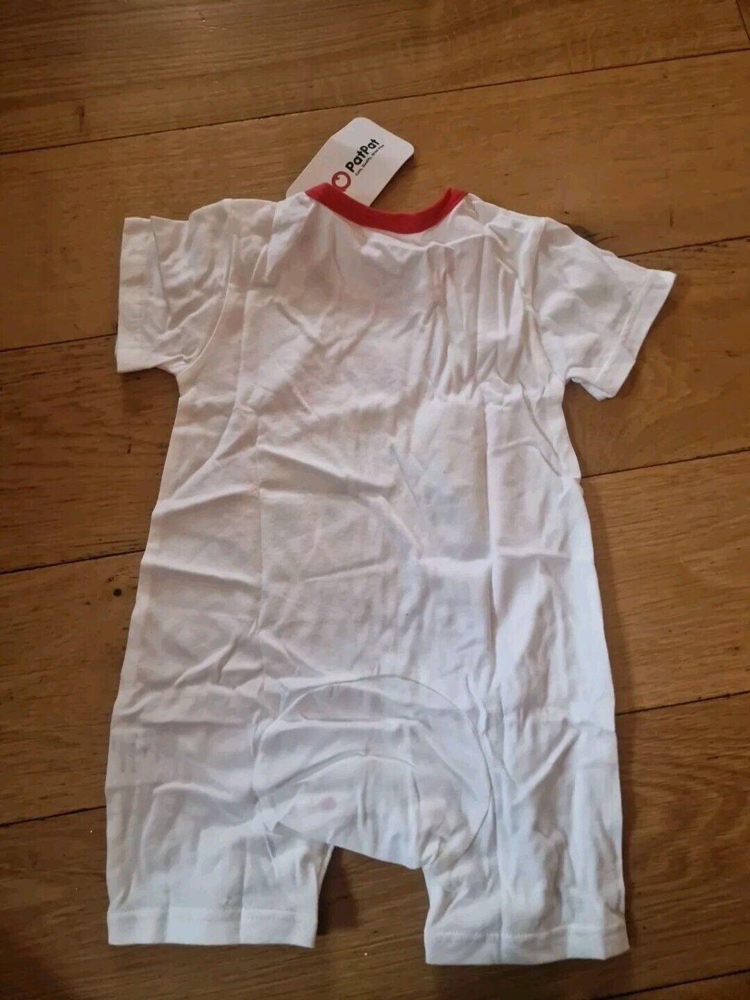 White baby romper 6-8 months with red neckline laid flat on wooden surface