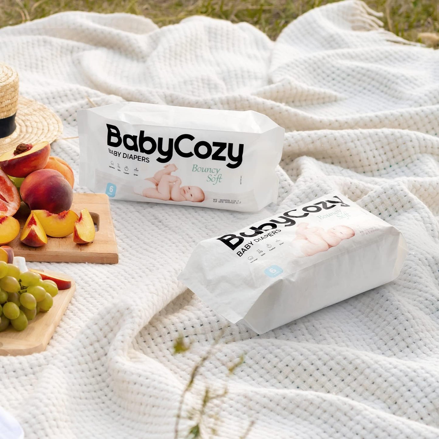 Two packs of Babycozy size 3 diapers on a picnic blanket with fresh fruits