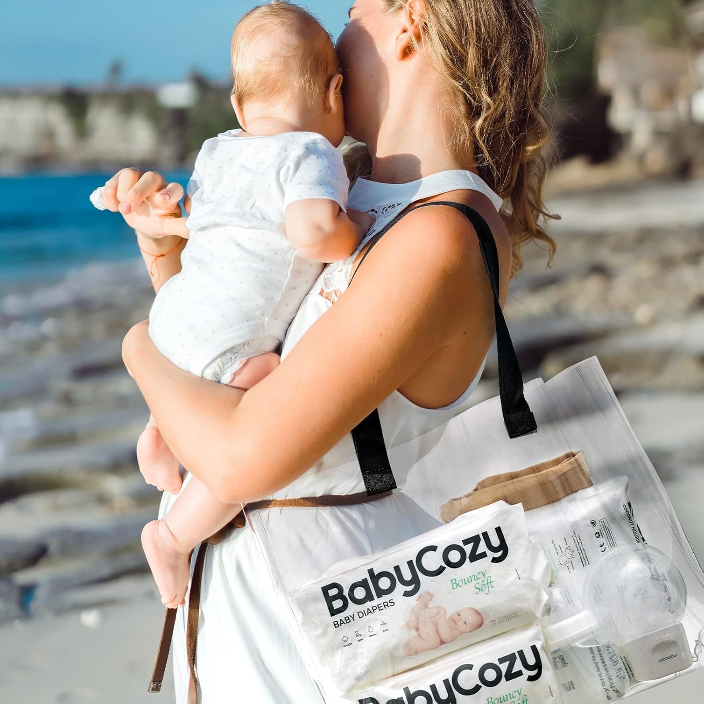 Mother holding baby by the beach with Babycozy size 3 diapers in a tote bag for convenient outings