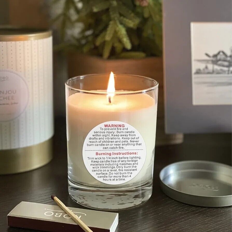 Candle warning label stickers on a glass candle with lit wick and decorative background