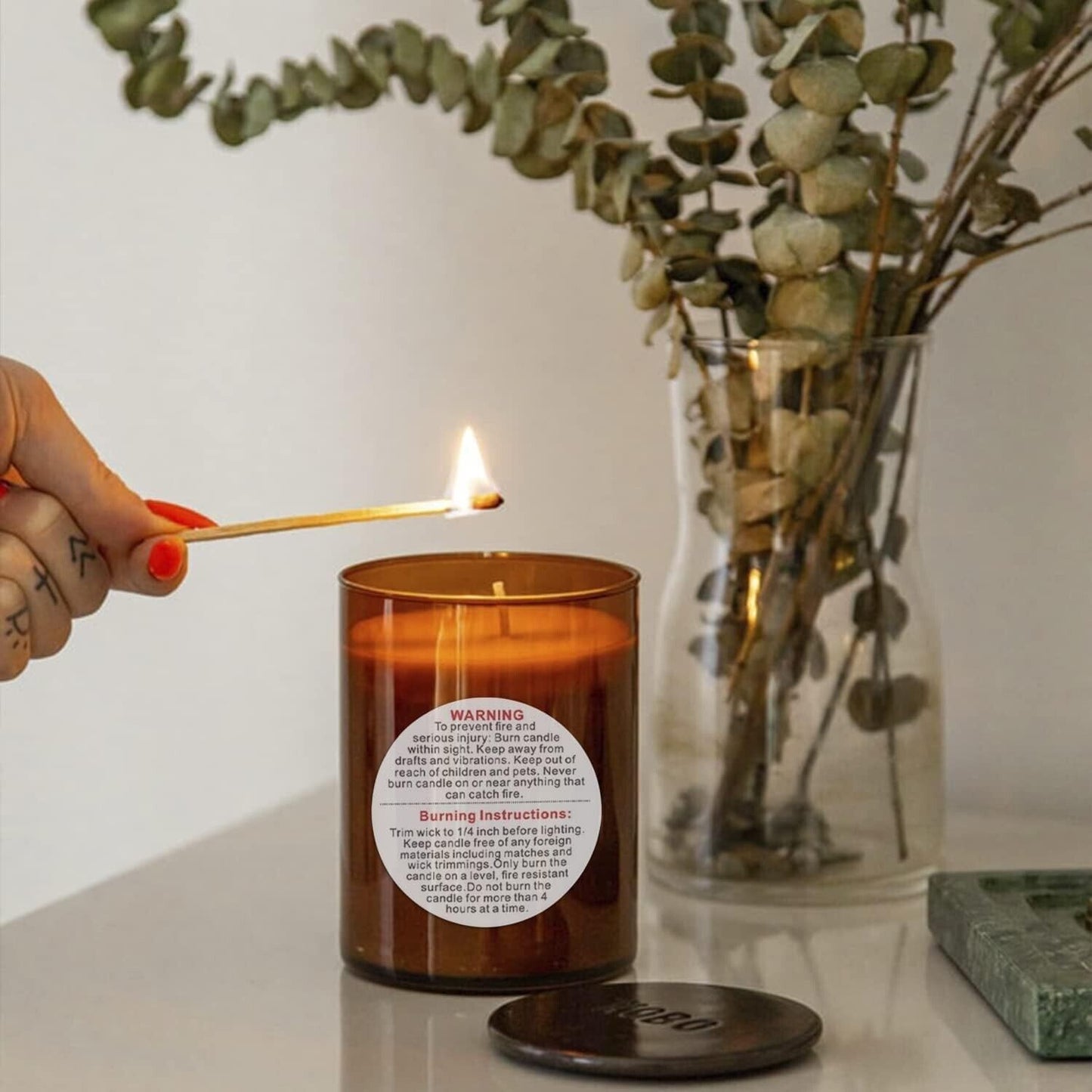 Candle warning label stickers on amber jar candle with match being lit in a stylish kitchen setting