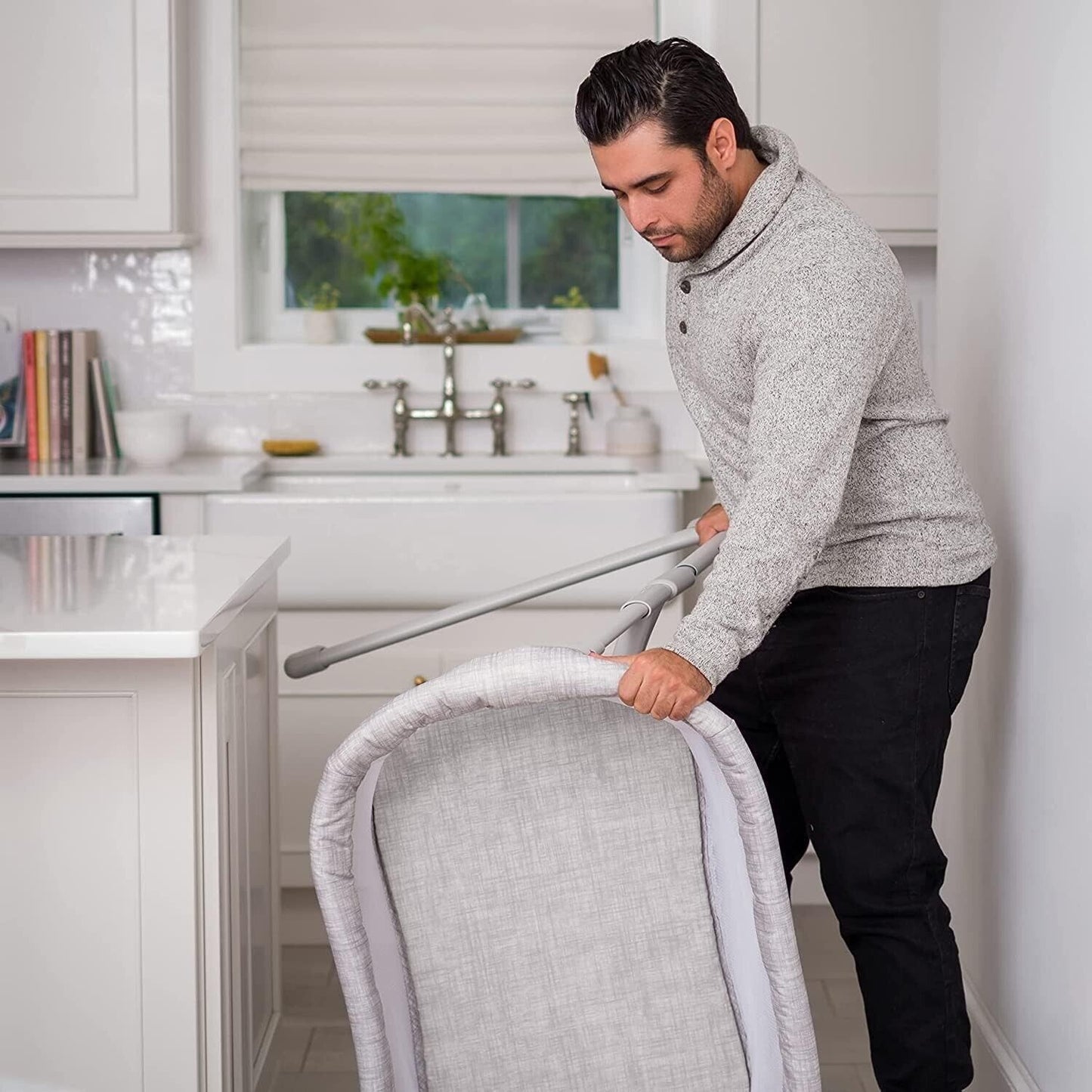 Man adjusting the Halo baby bassinet sleeper in a modern kitchen for a safe sleep environment