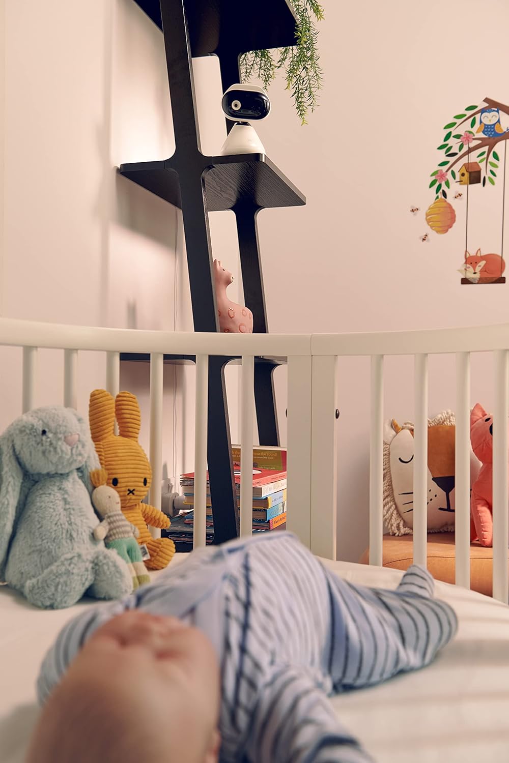 Motorola video baby monitor positioned above a crib in a nursery with plush toys and a sleeping baby