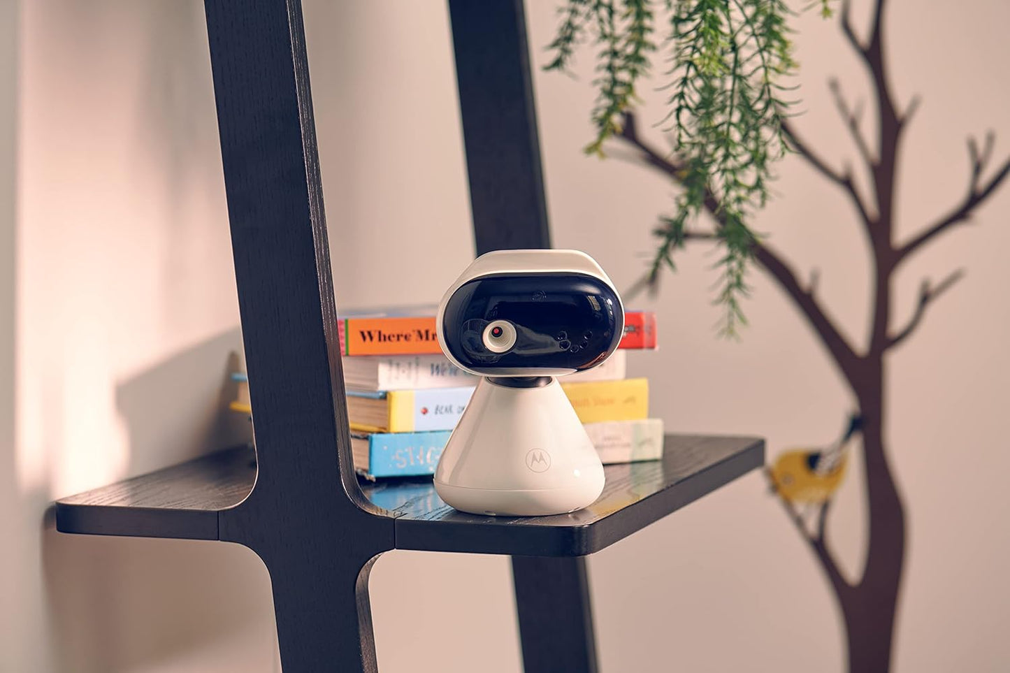 Motorola video baby monitor on a shelf with colourful books and a decorative tree wall decal