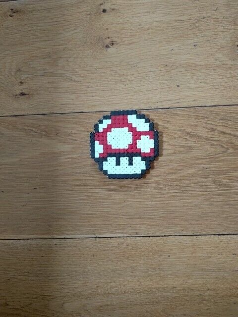 Super Mario mushroom perler bead ornament on a wooden surface, vibrant red and white design