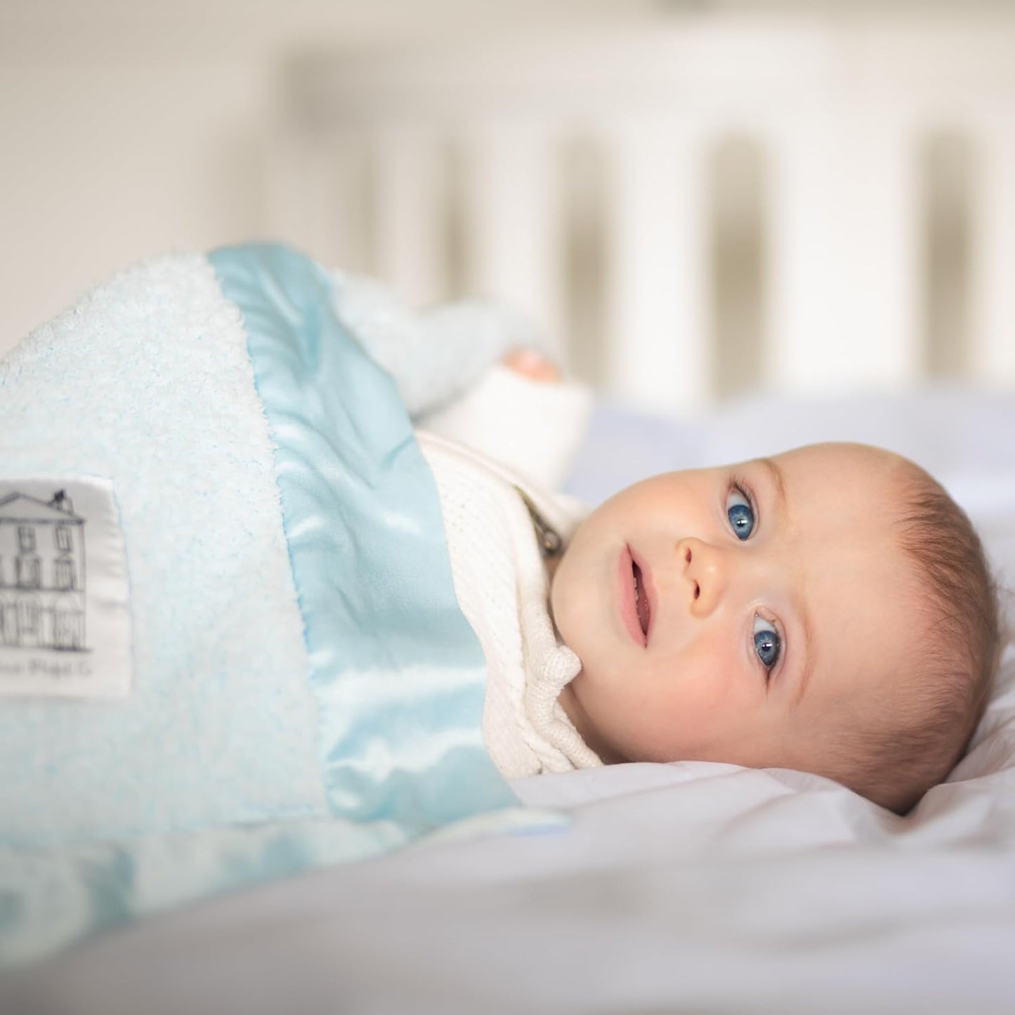 Infant snuggled in a blue baby chenille blanket on a bed with soft bedding