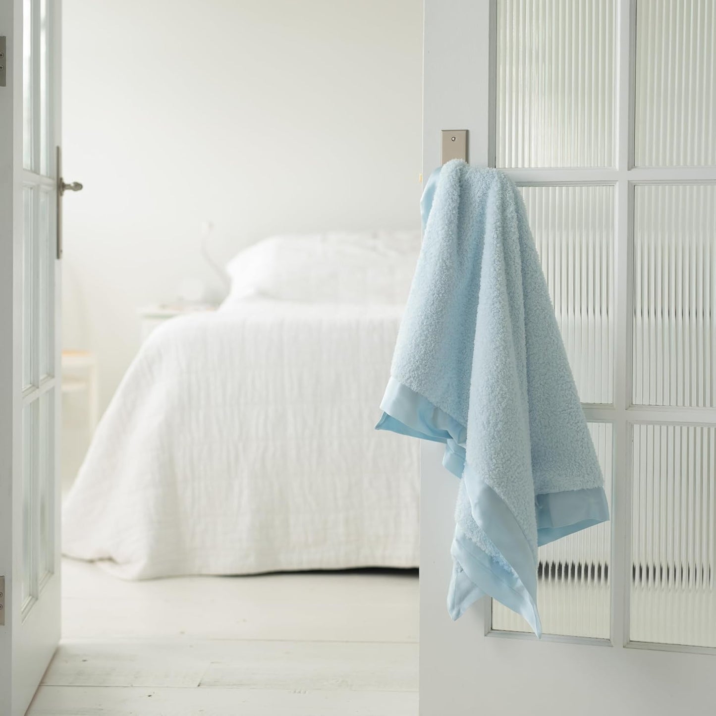 Soft baby blue baby chenille blanket draped over a door handle in a bright, minimalist room