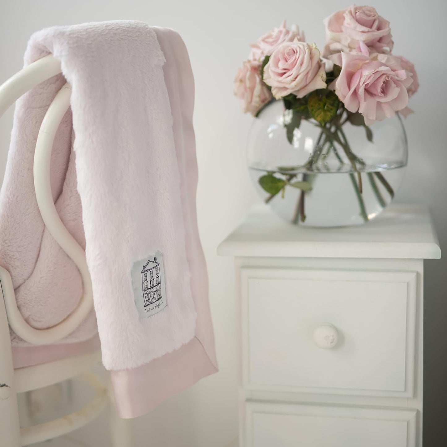 Soft pink baby chenille blanket draped over a chair next to a vase of pink roses