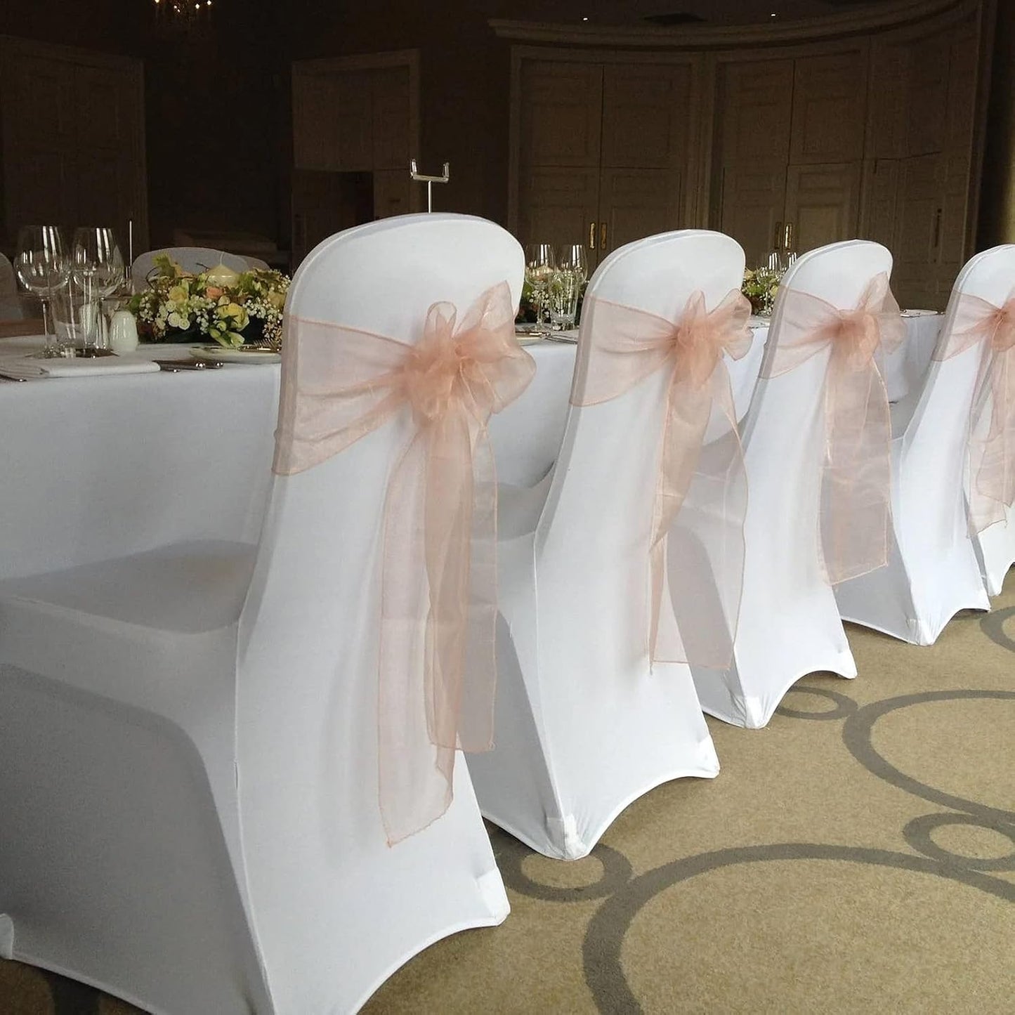Elegant white polyester stretch chair covers with soft peach sashes for stylish event decor