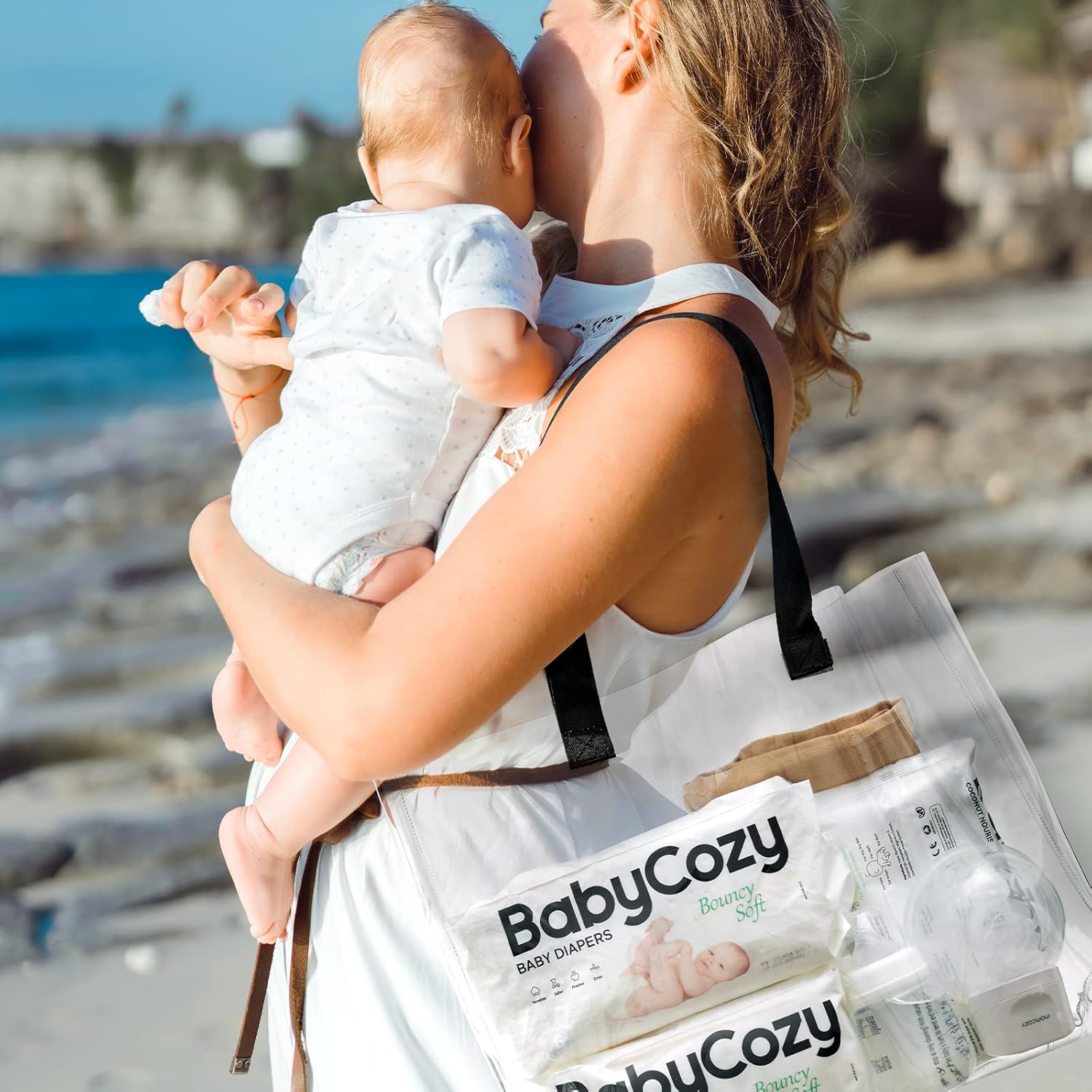 Mother holding baby by the beach with Babycozy size 3 diapers in a tote bag for convenient outings