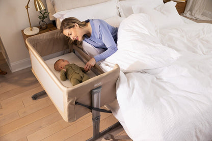 GRACO bedside crib for newborns positioned next to a bed, with a mother interacting with her baby