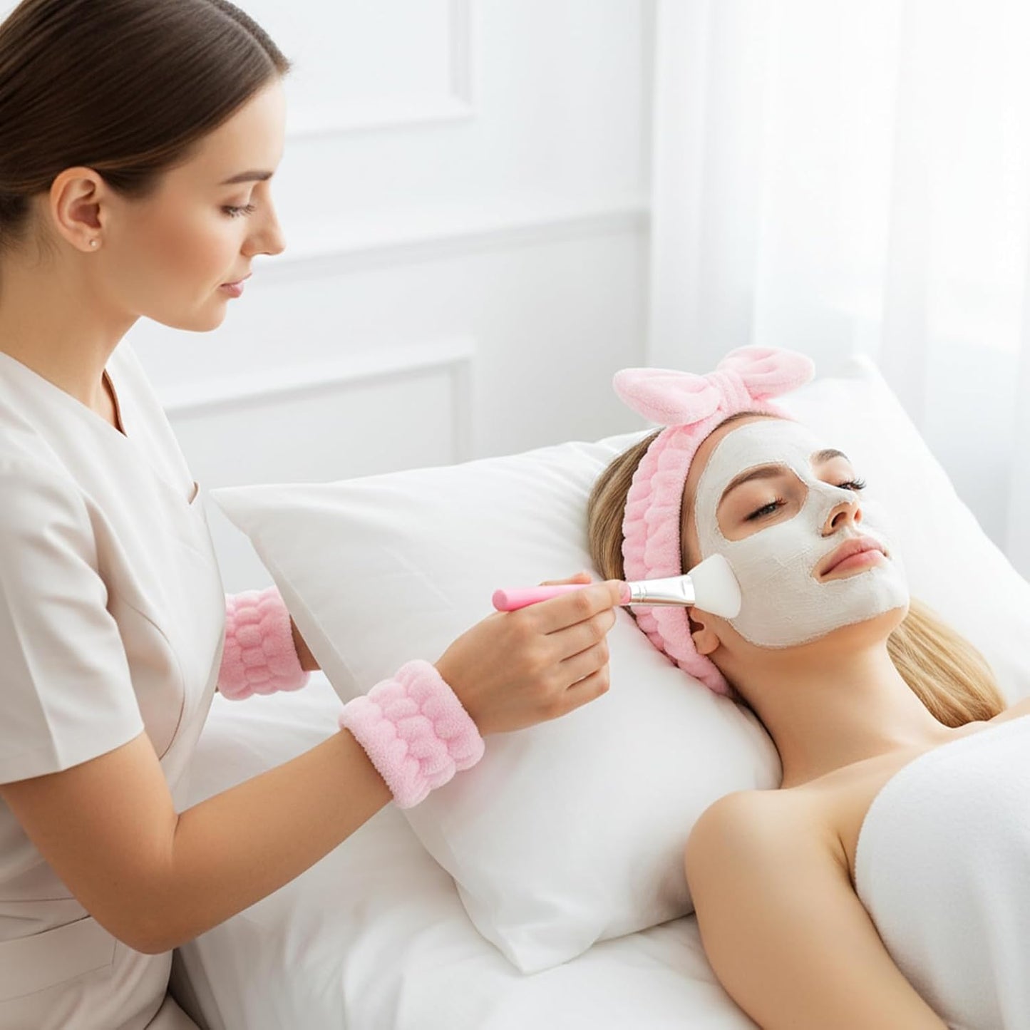 Woman applying a facial mask with a brush while using a gua sha for skincare treatment