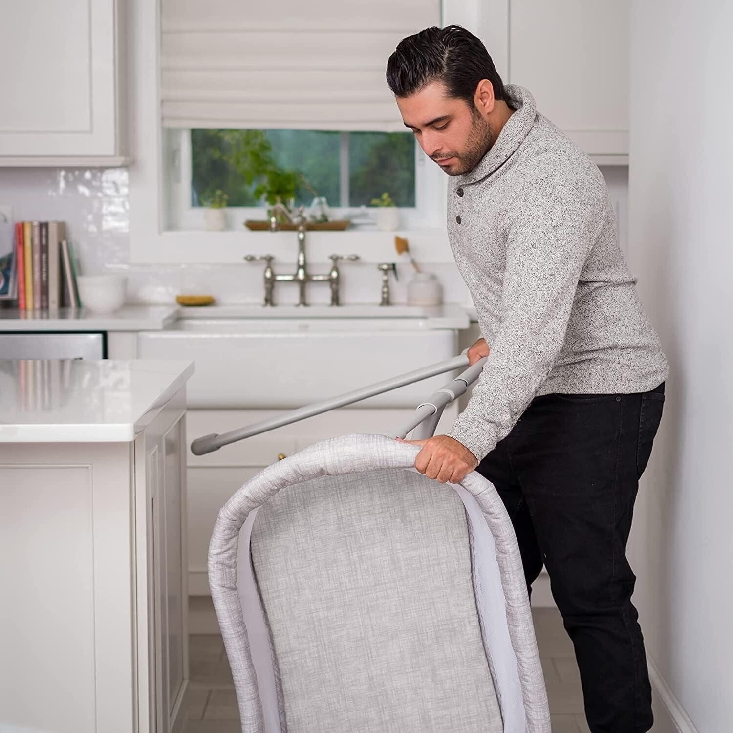 Man adjusting the Halo baby bassinet sleeper in a modern kitchen for a safe sleep environment