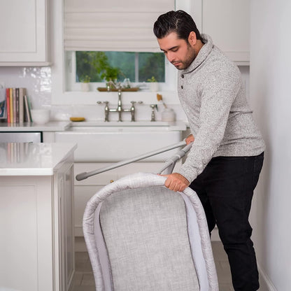 Man adjusting the Halo baby bassinet sleeper in a modern kitchen for a safe sleep environment