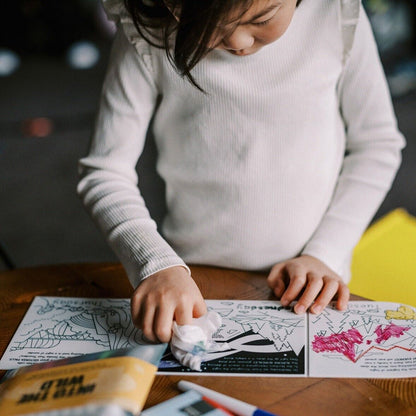 Child engaging with HeyDoodle Tales Natural Wonders activity book, colouring with crayons at a table