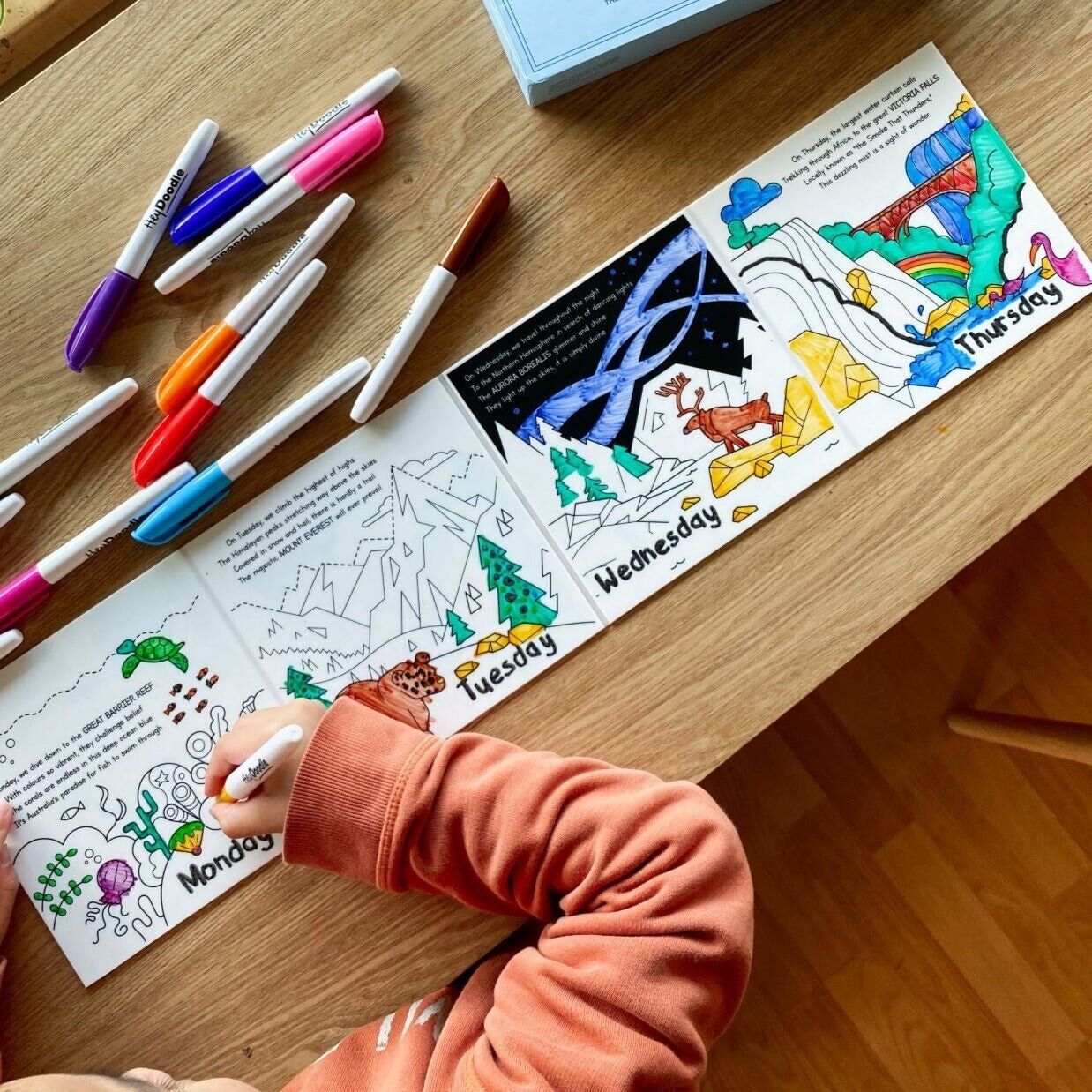 HeyDoodle Tales Natural Wonders activity book opened with colourful markers on a wooden table