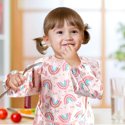 Cute toddler wearing long sleeve weaning bibs with colourful rainbow print while enjoying mealtime