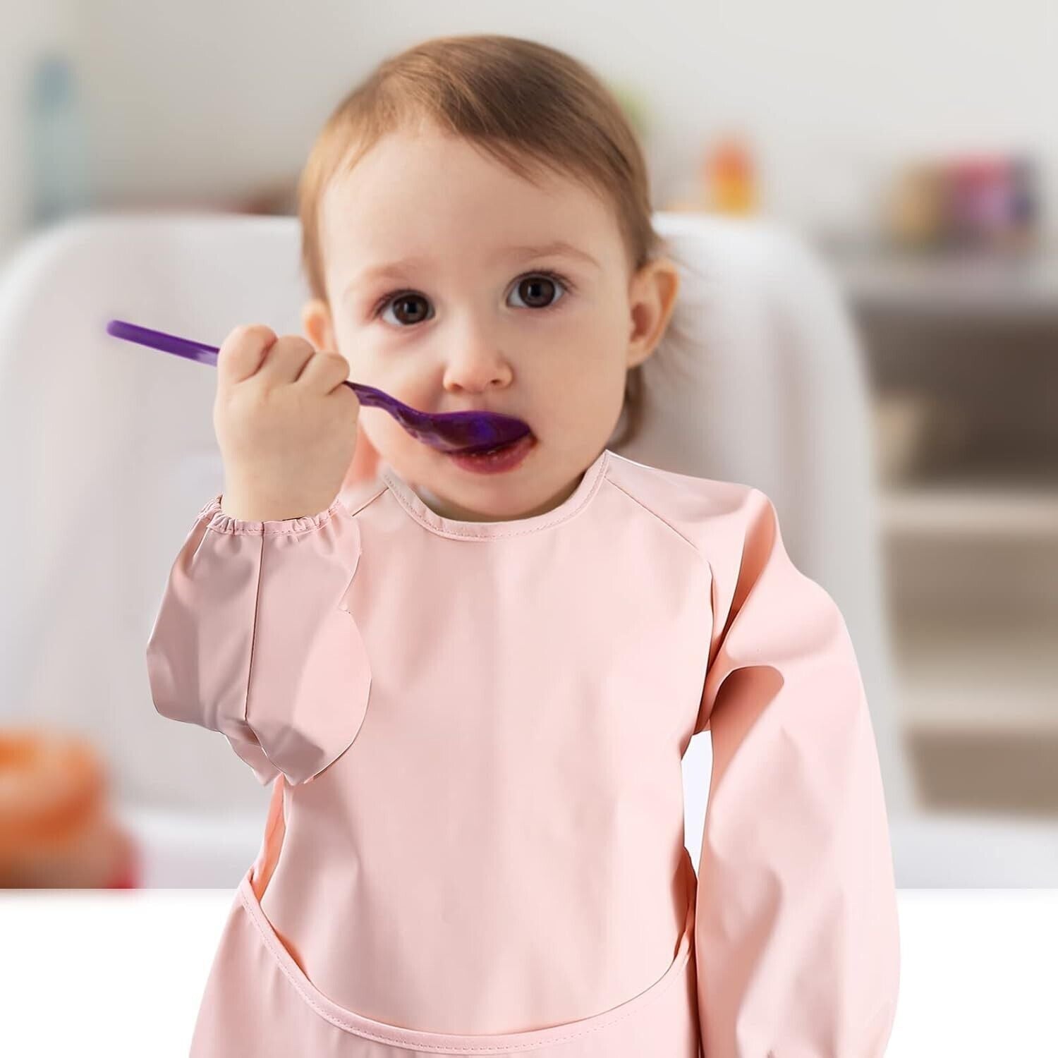 Toddler wearing a pink long sleeve weaning bibs, enjoying food with a spoon during mealtime