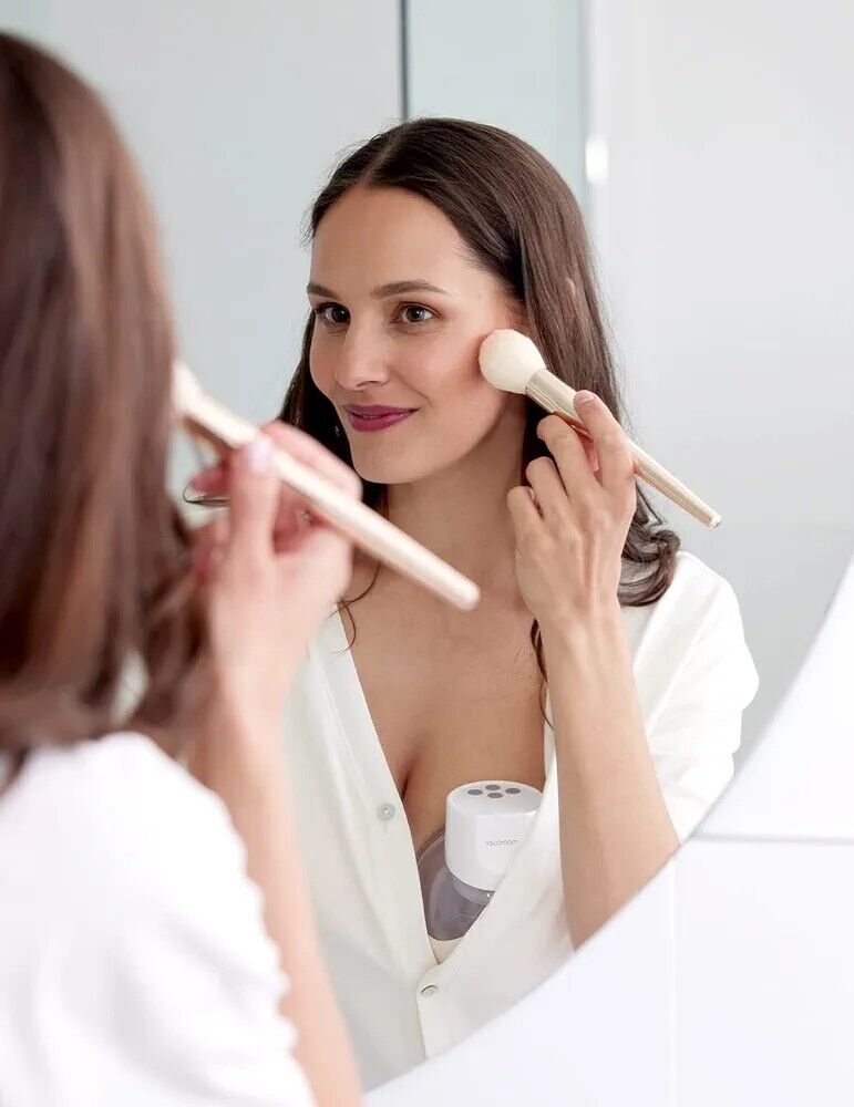 Woman applying blush in front of mirror with Momcozy S12 Pro wearable breast pump discreetly visible