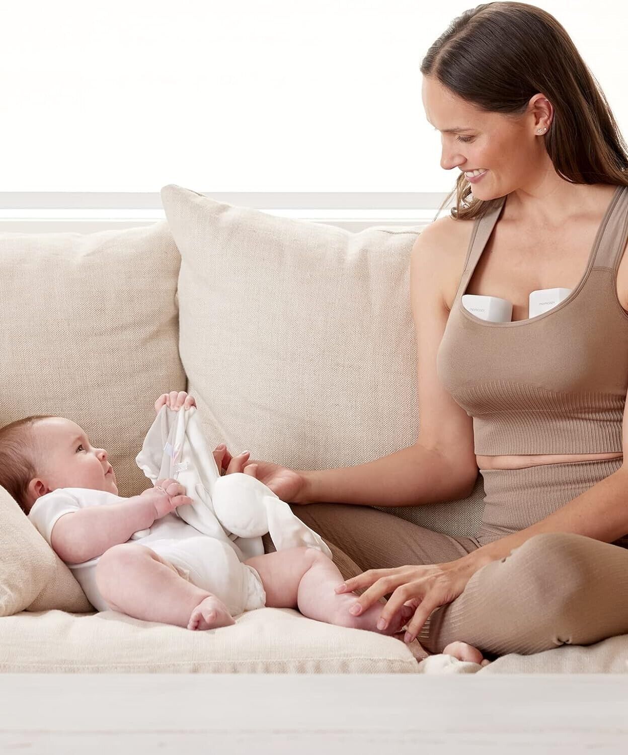 Momcozy S12 Pro wearable breast pump in use while a mother comfortably interacts with her baby on the couch