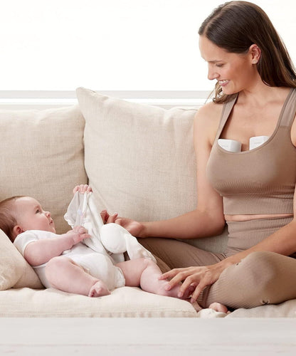 Momcozy S12 Pro wearable breast pump in use while a mother comfortably interacts with her baby on the couch