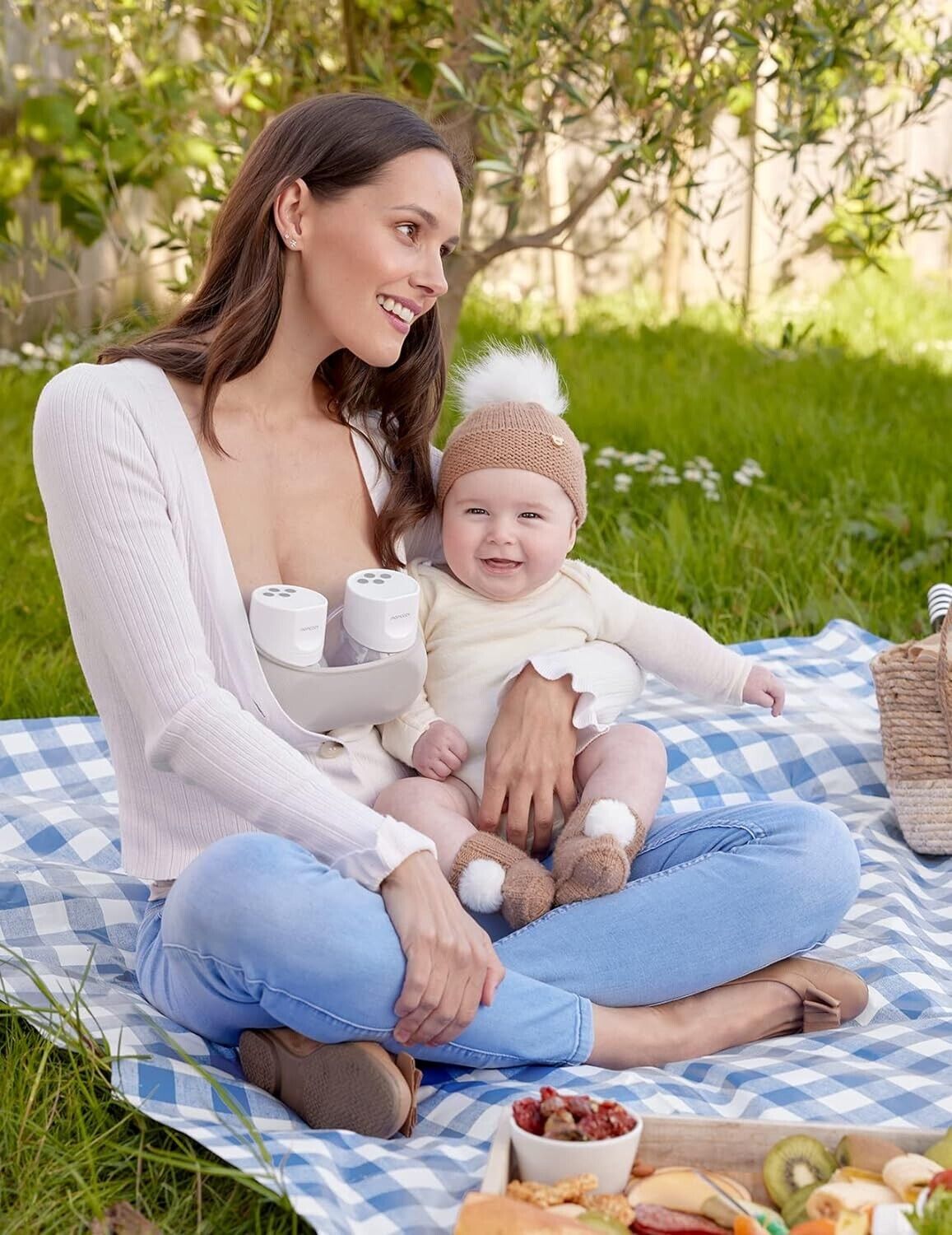 Momcozy S12 Pro wearable breast pump in use by a mother at a picnic with her baby on a grassy area