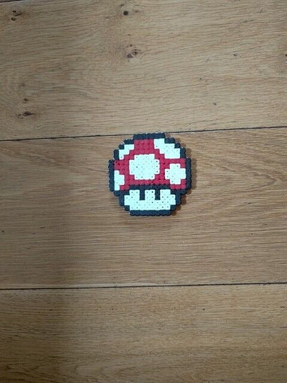 Super Mario mushroom perler bead ornament on a wooden surface, vibrant red and white design