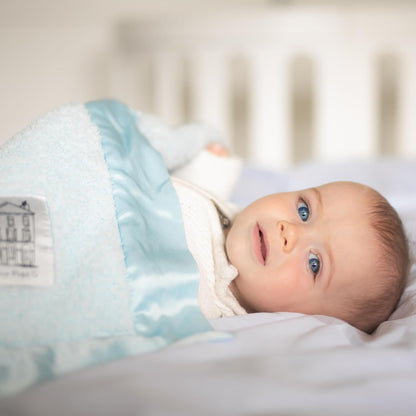 Infant snuggled in a blue baby chenille blanket on a bed with soft bedding