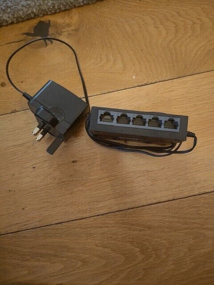TP-LINK 5 port gigabit switch with power adapter on a wooden surface